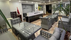 A reception area with a sign, wicker furniture, and a clock. - Kartel Hotel (Didim)