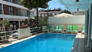 A swimming pool with a tiled deck, green lounge chairs, and a tree. - Kartel Hotel (Didim)