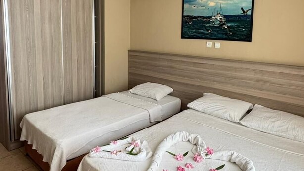 A hotel room with two beds, a painting of a boat on the wall, and a ceiling light. - Kartel Hotel (Didim)