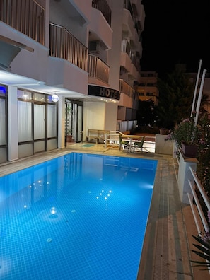 A hotel with a swimming pool, outdoor seating, and a balcony with railings.