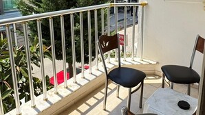A balcony with two chairs and a table, overlooking a building with multiple floors and a tree. - Kartel Hotel (Didim)