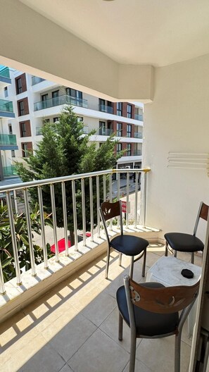 A balcony with two chairs and a table, overlooking a building with multiple floors and a tree. - Kartel Hotel (Didim)