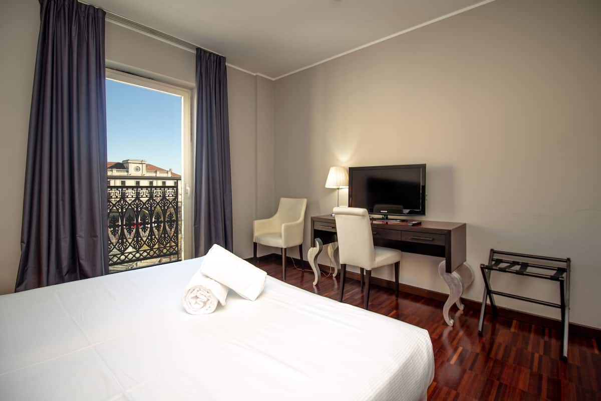 A hotel room with a bed, a desk, a chair, a TV, and a window with curtains.