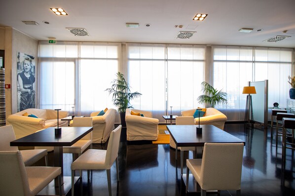 Eine moderne Hotelhalle mit weißen Sofas, einem Essbereich und großen Fenstern, die für natürliches Licht sorgen.