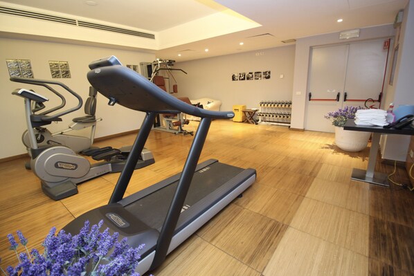 A gym with exercise equipment, a treadmill, and a wall-mounted rack of dumbbells.