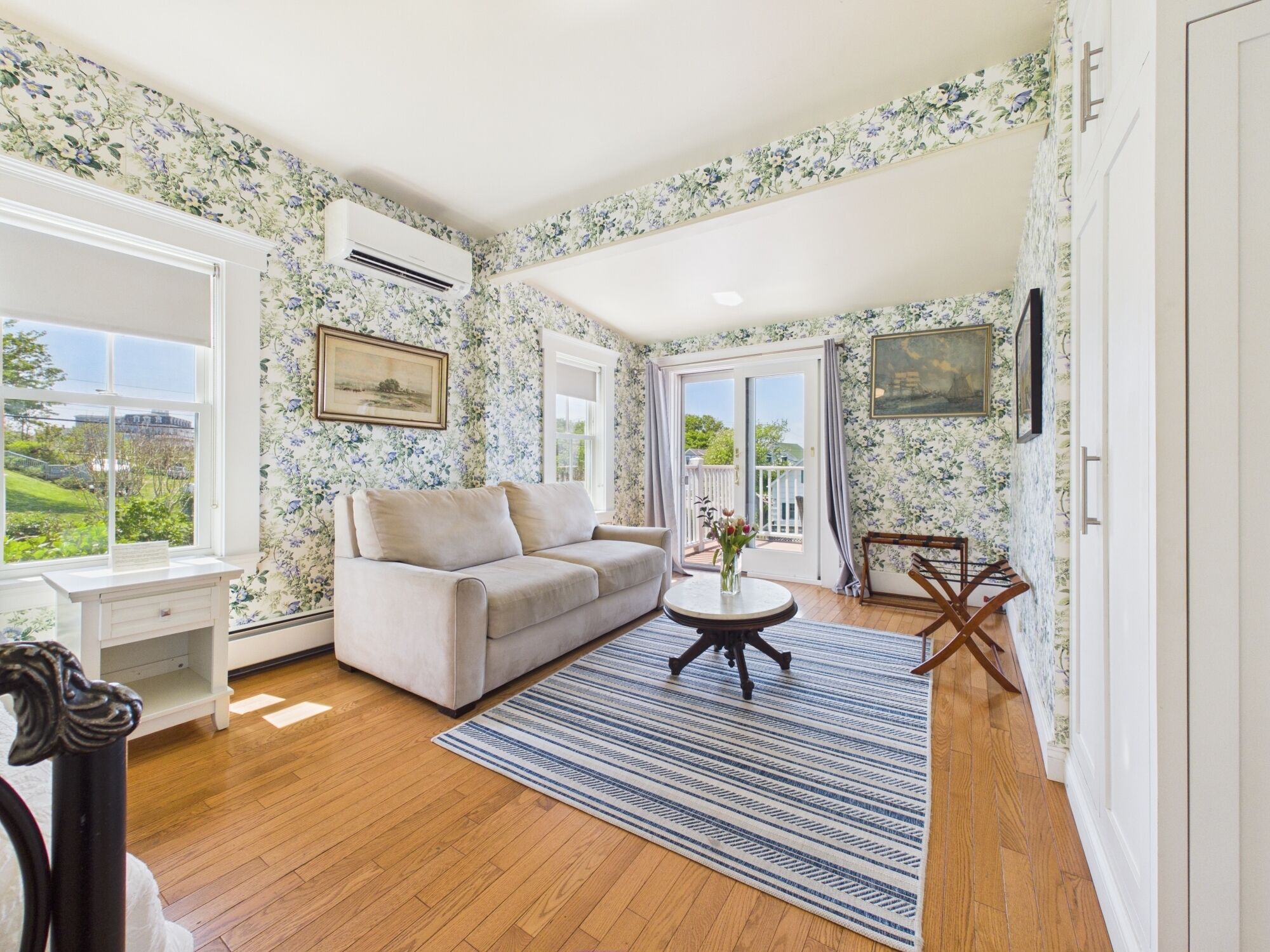 A living room with floral wallpaper, a sofa, a coffee table, and a view through a window.