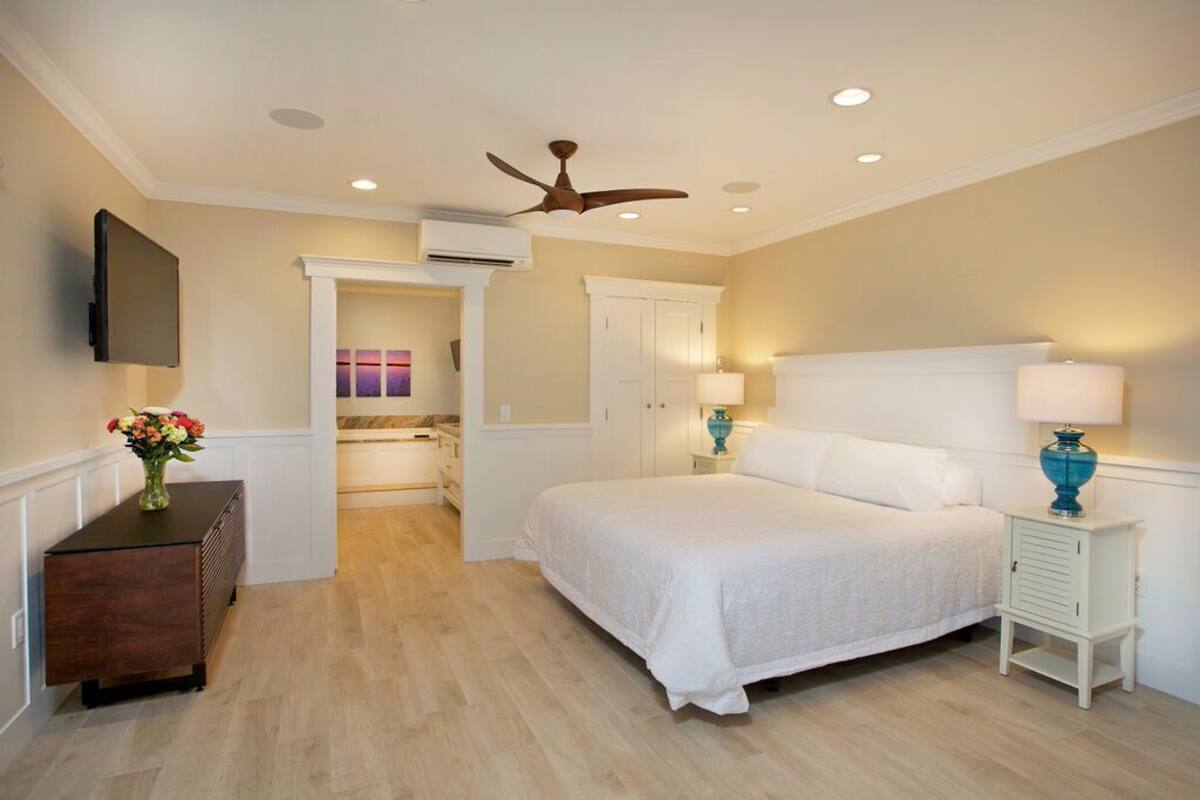 A bedroom with a bed, bedside tables, a ceiling fan, and a TV mounted on the wall.
