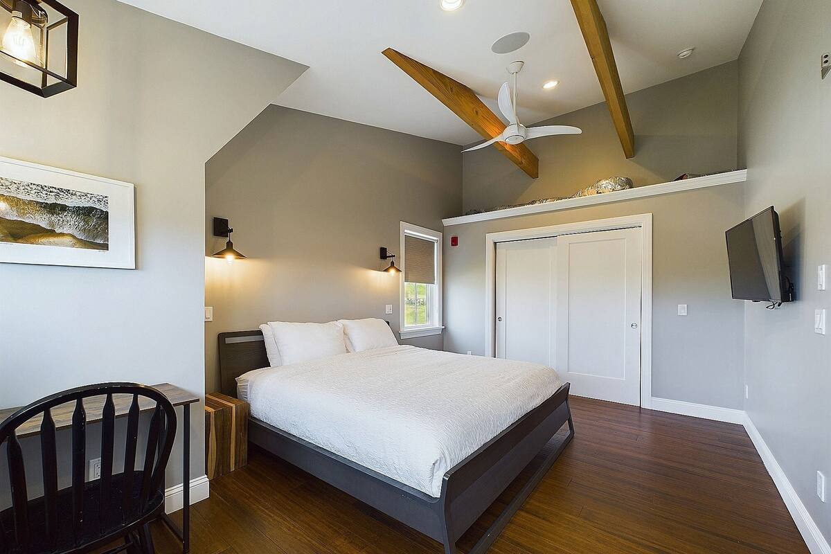 A bedroom with a bed, a chair, a ceiling fan, a TV, and a door.