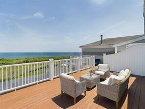 A deck with wicker furniture and a white railing overlooking the ocean.