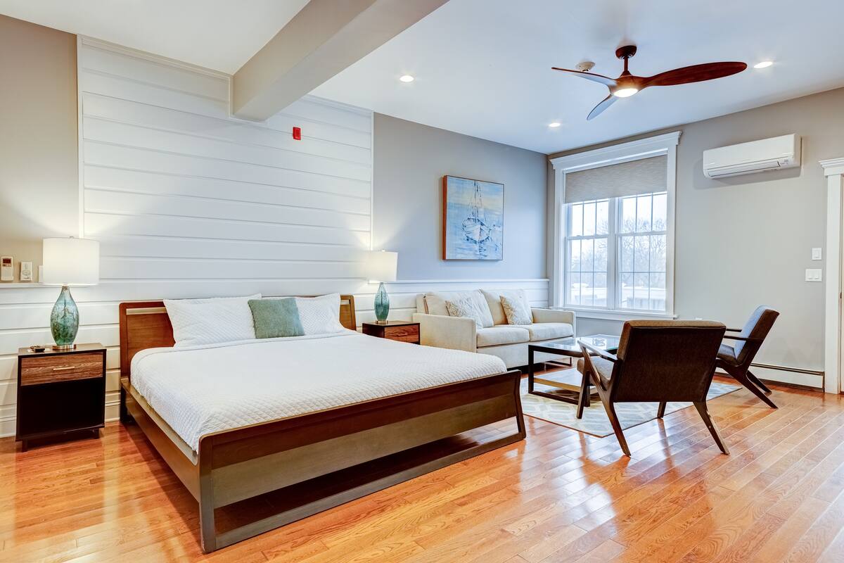 A modern bedroom with a large bed, a ceiling fan, a sofa, and a dining table.