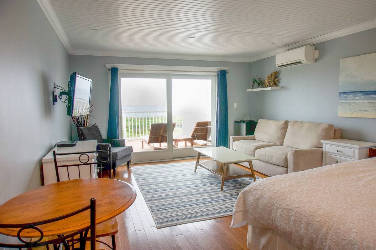 A room with a bed, a sofa, a dining table, and a balcony with chairs.