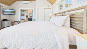 A bedroom with a wooden ceiling, a large bed, a TV on the wall, and a window with a view. - The 1661 Inn (Block Island)
