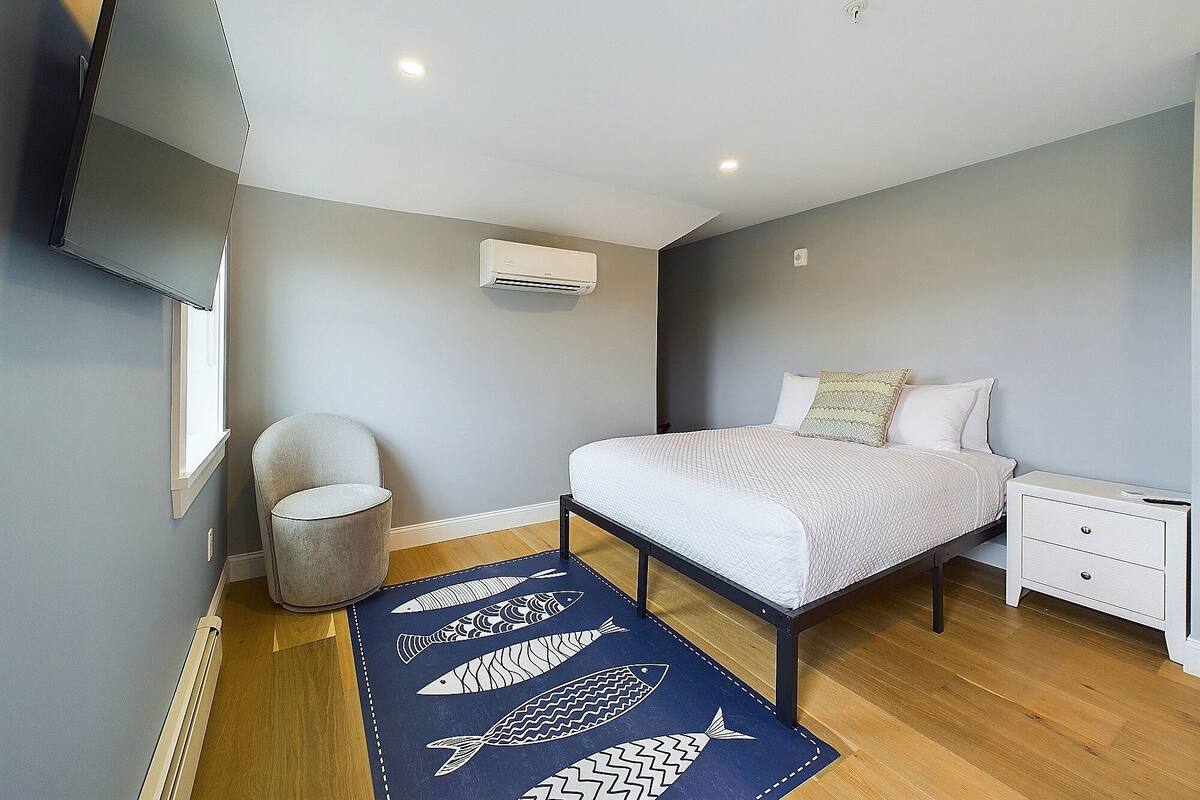 Een slaapkamer met een bed, nachtkastje, stoel en een blauw vloerkleed met vismotieven.