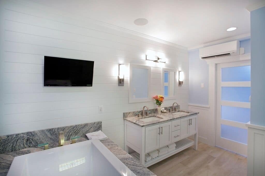 A modern bathroom with a large bathtub, double vanity with a mirror, and a mounted TV.