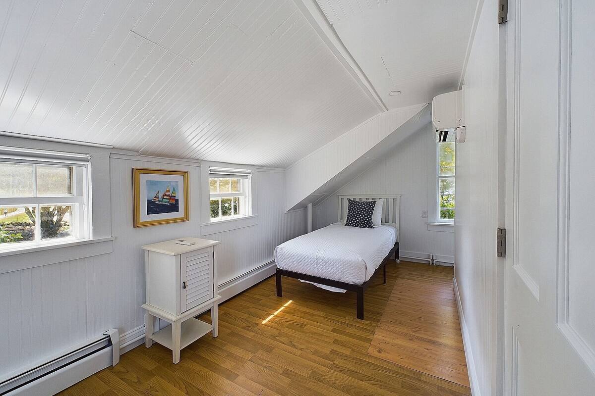 Een slaapkamer met een schuine kap, een bed, een radiator en een raam met uitzicht.
