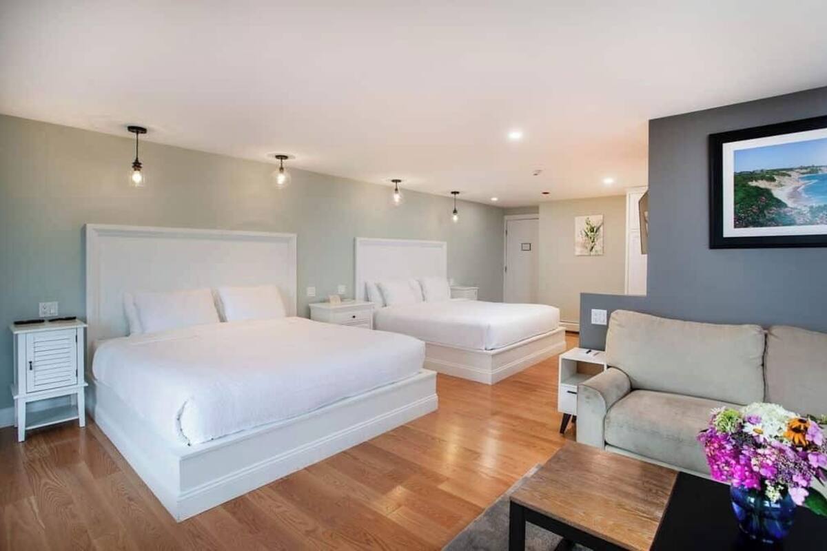 A bedroom with two beds, a sofa, a coffee table, and a painting on the wall.