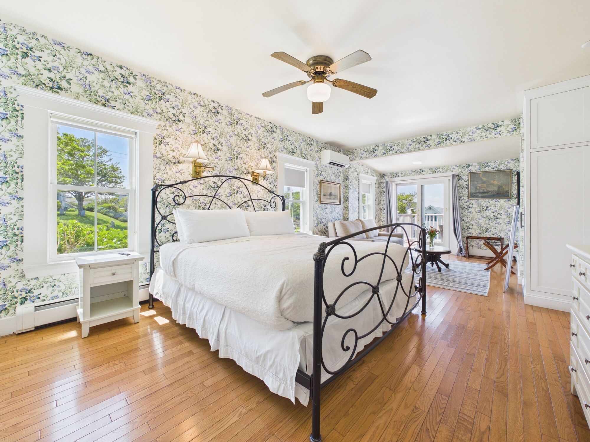 A bedroom with a bed, a nightstand, a ceiling fan, and a view of the outdoors.