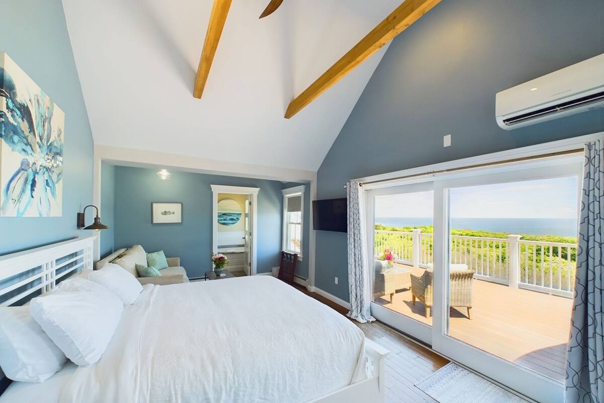 A bedroom with a bed, a TV, and a balcony with a view.