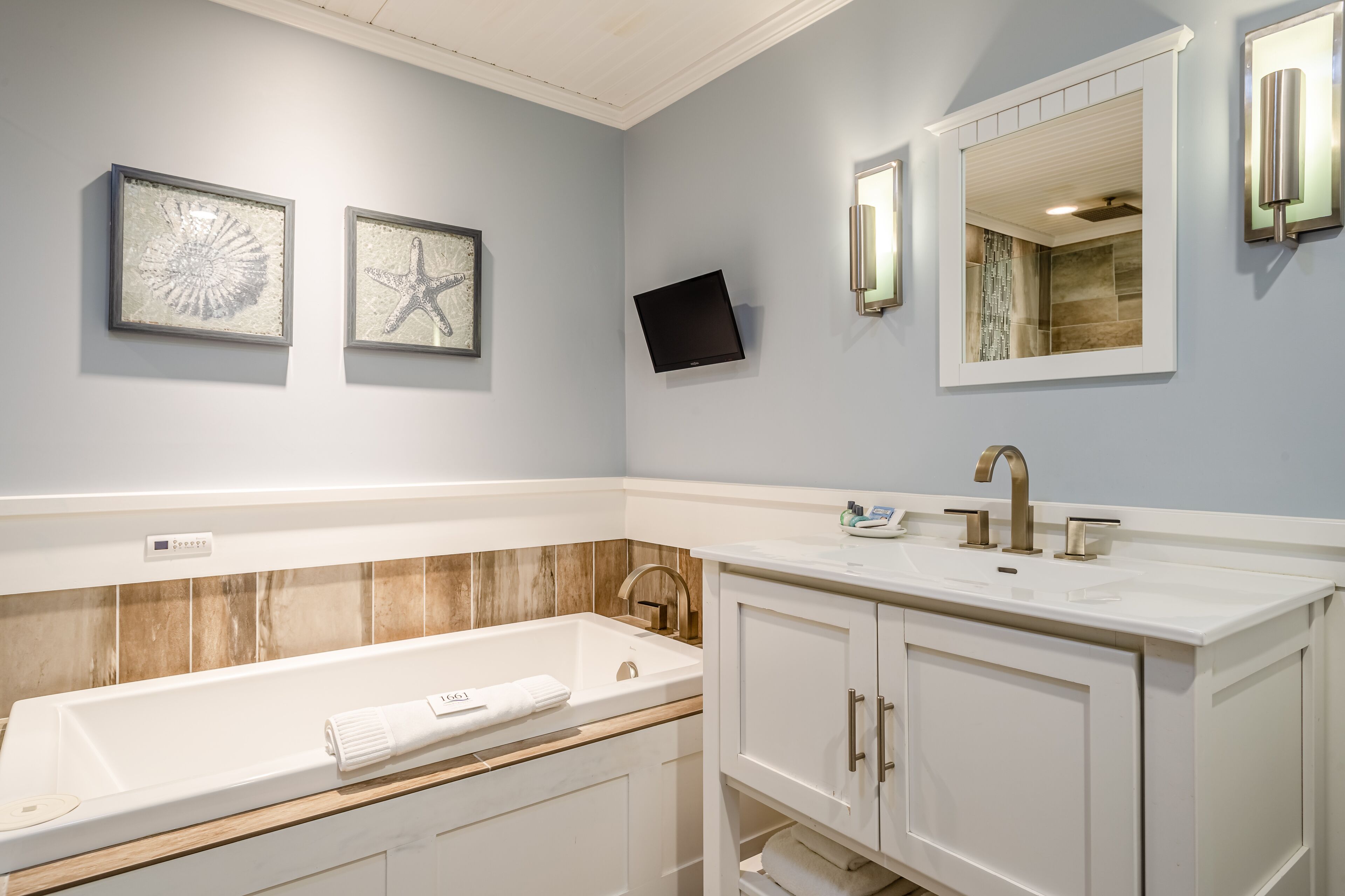 A modern bathroom with a freestanding bathtub, a vanity with a sink, and two framed artworks on the wall.