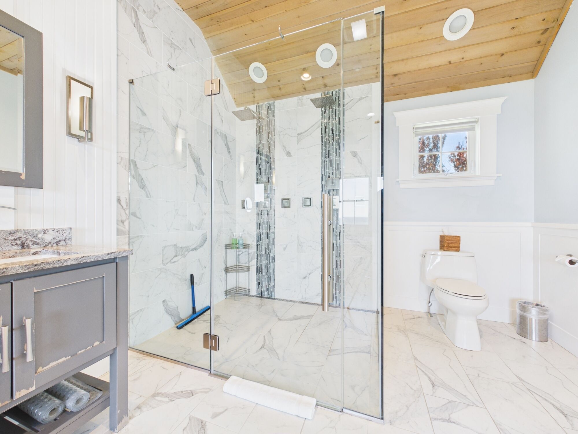 A modern bathroom with a glass-enclosed shower, marble flooring, and a wooden ceiling.