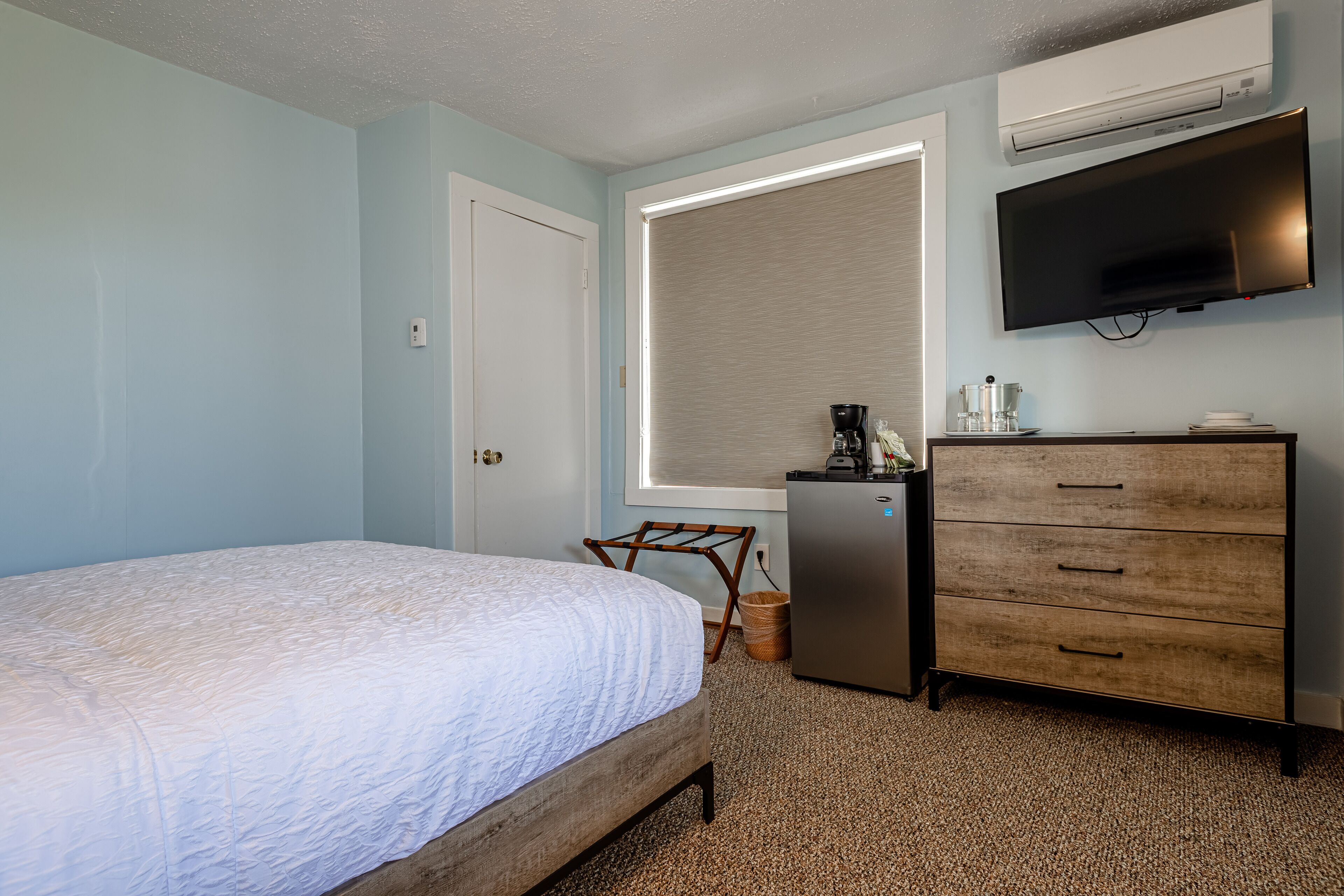 A bedroom with a bed, a dresser, a television, and a window with blinds.