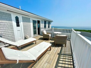 A wooden deck with two sun loungers, a wicker chair, and a small round table.