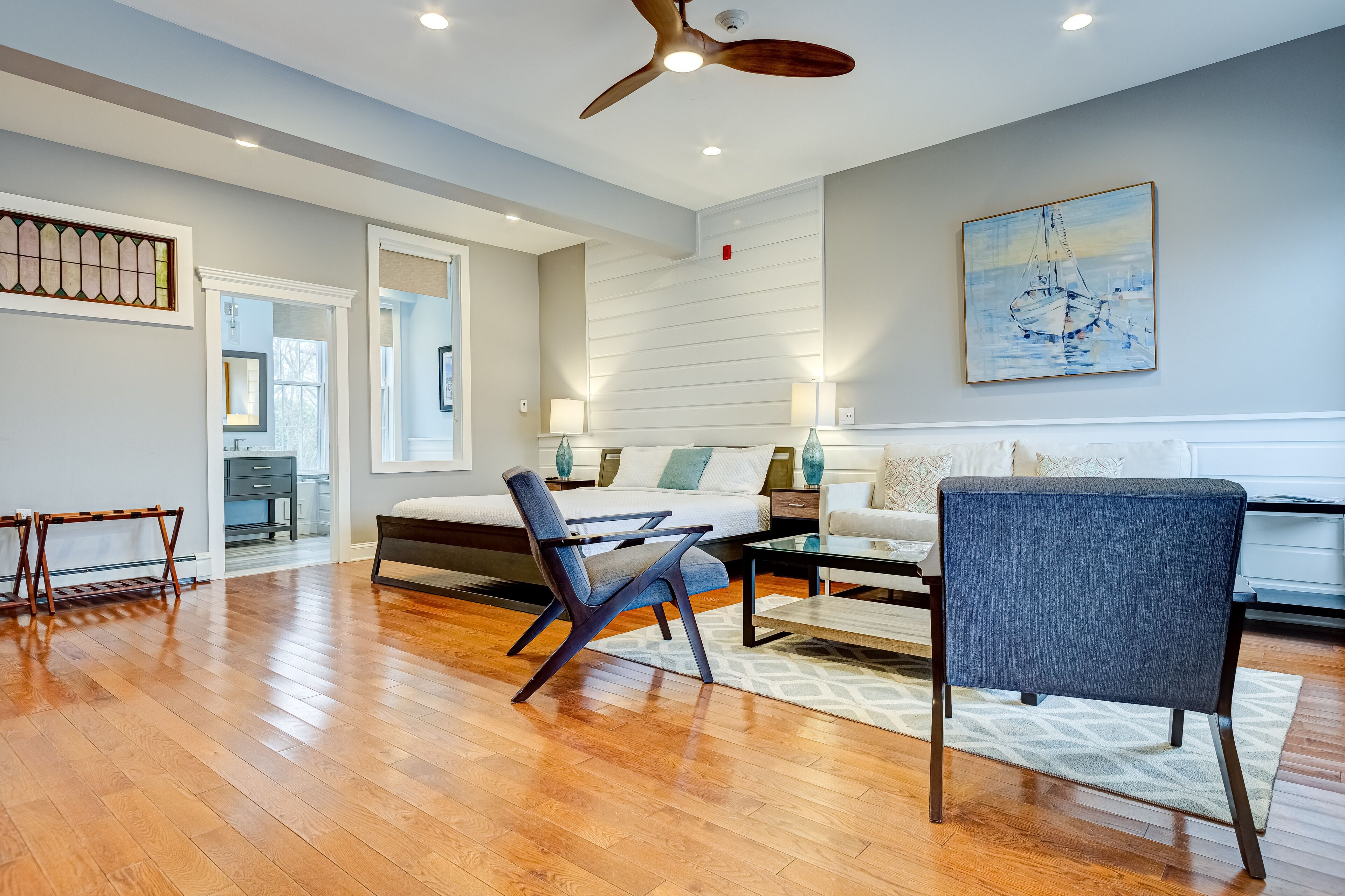 A spacious living room with a wooden floor, a ceiling fan, a sofa, a coffee table, and a painting on the wall.