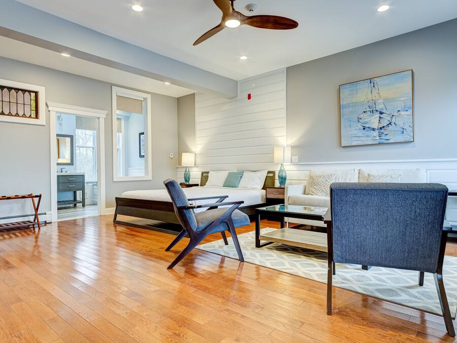 A spacious living room with a wooden floor, a ceiling fan, a sofa, a coffee table, and a painting on the wall.