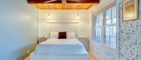 Un dormitorio con techo de madera, una cama, dos mesitas de noche, una ventana y una pared con estampado floral.