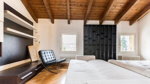 Ein Schlafzimmer mit Holzbalkendecke, einem Bett, einem Sessel, einer Kommode und einem Heizkörper.