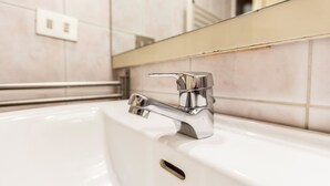 Ein modernes Badezimmer mit einem chromfarbenen Wasserhahn, einem weißen Waschbecken und einem Spiegel darüber.