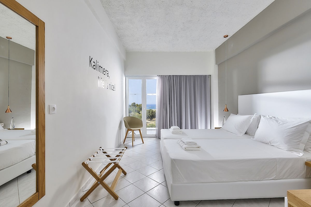 Een moderne hotelkamer met twee bedden, een grote spiegel en uitzicht op zee.
