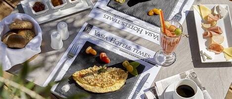 Une table mise pour le petit-déjeuner avec un journal, une assiette de charcuterie, un verre de jus de fruits et un bol de pain.