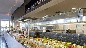 Un buffet proposant une variété de plats et de boissons, un coin cuisine à l’arrière-plan et un aménagement intérieur moderne.