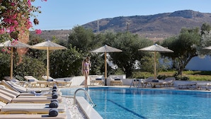 Un espace piscine doté de chaises longues et de parasols, entouré de verdure et avec une montagne en toile de fond.