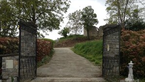 Un camino pavimentado que conduce a una entrada con puerta, un muro de piedra y un poste blanco.