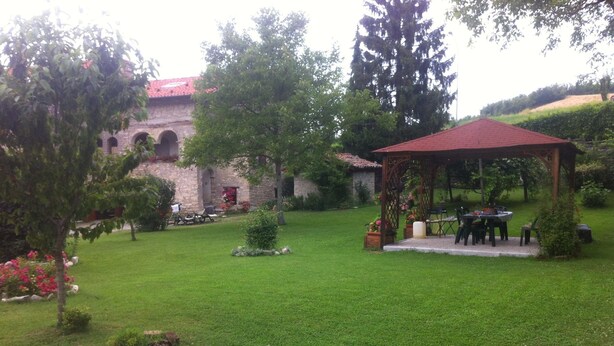 Un jardín con un pabellón, edificio de piedra y abundante vegetación.