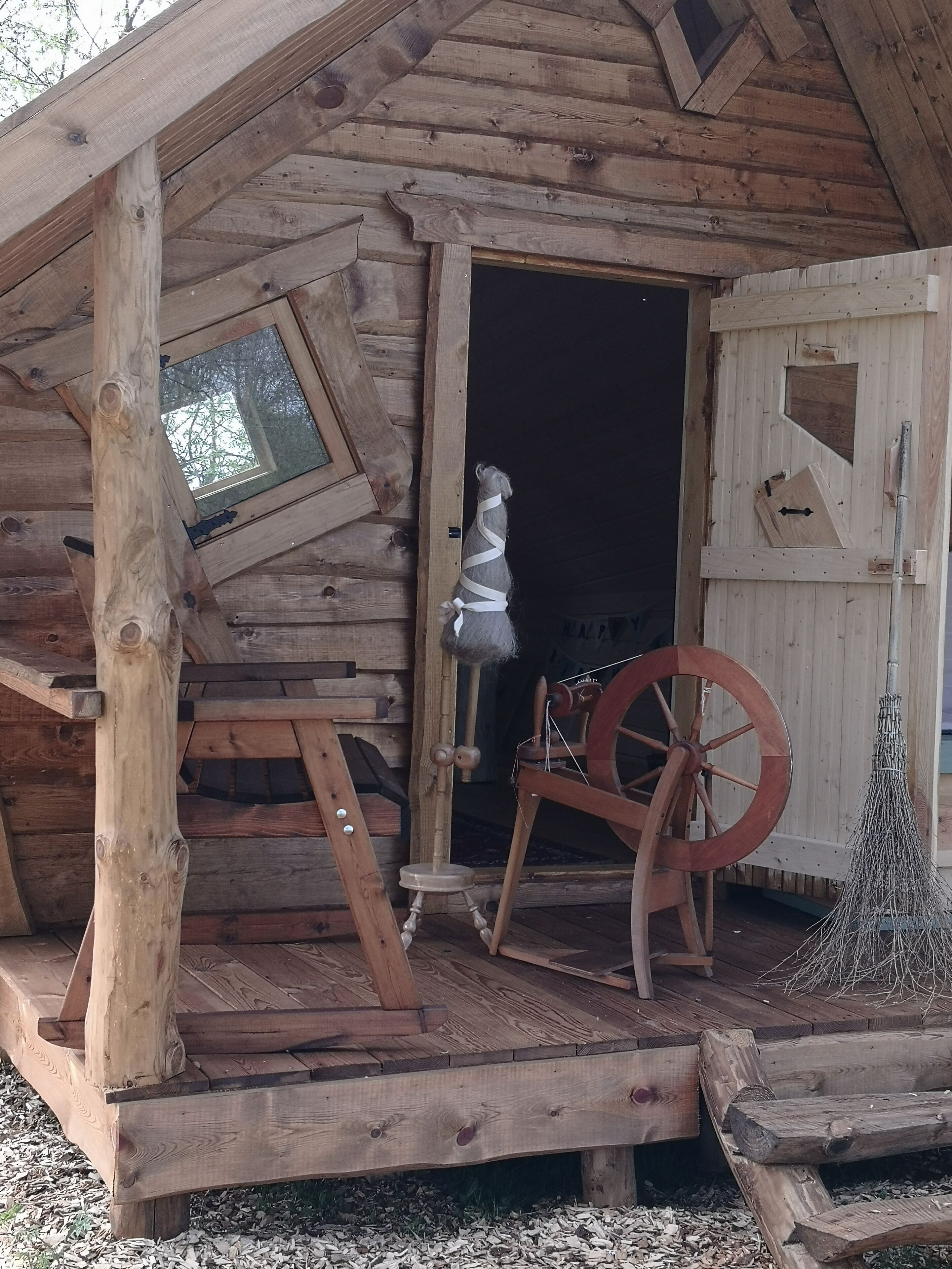 A rustic wooden cabin with a porch, a spinning wheel, and a small window.