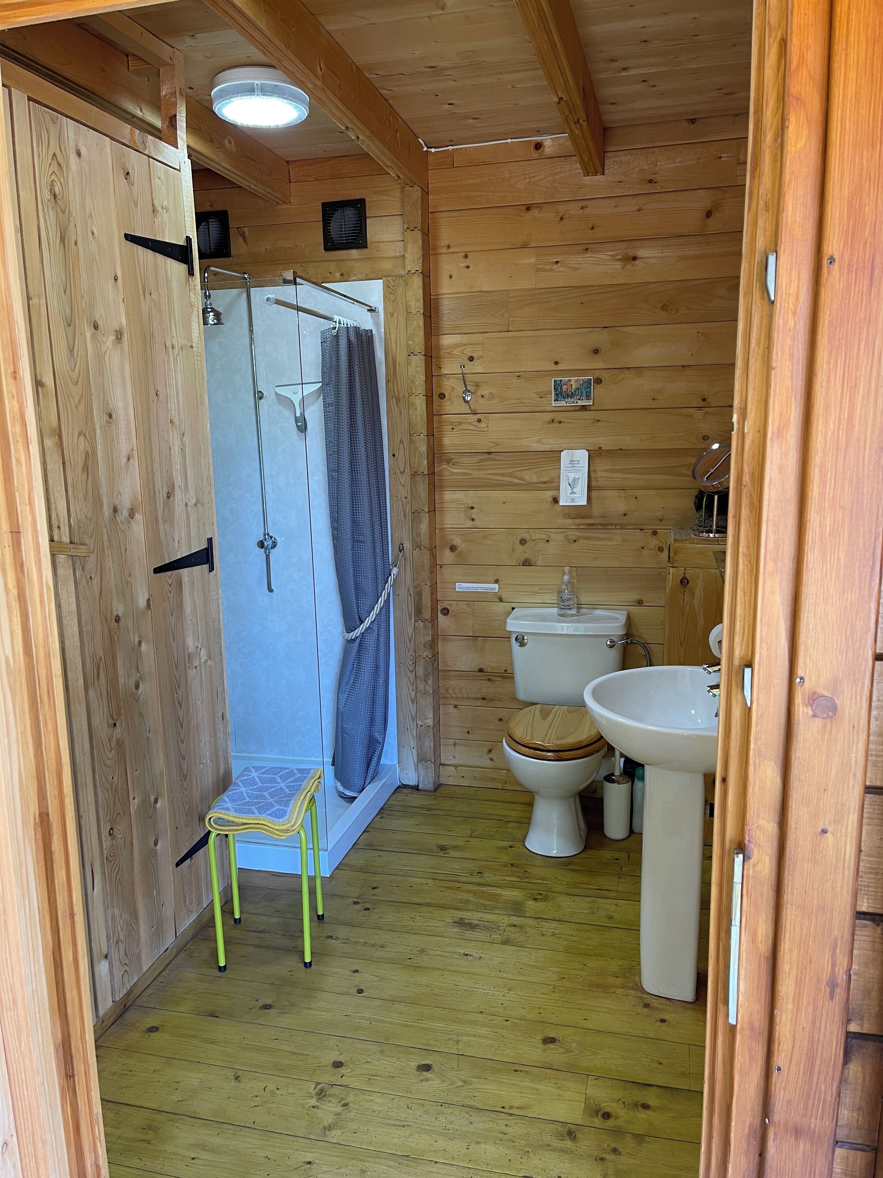 Une salle de bain rustique, aménagée dans une cabane en bois, avec une douche, des toilettes et un lavabo.
