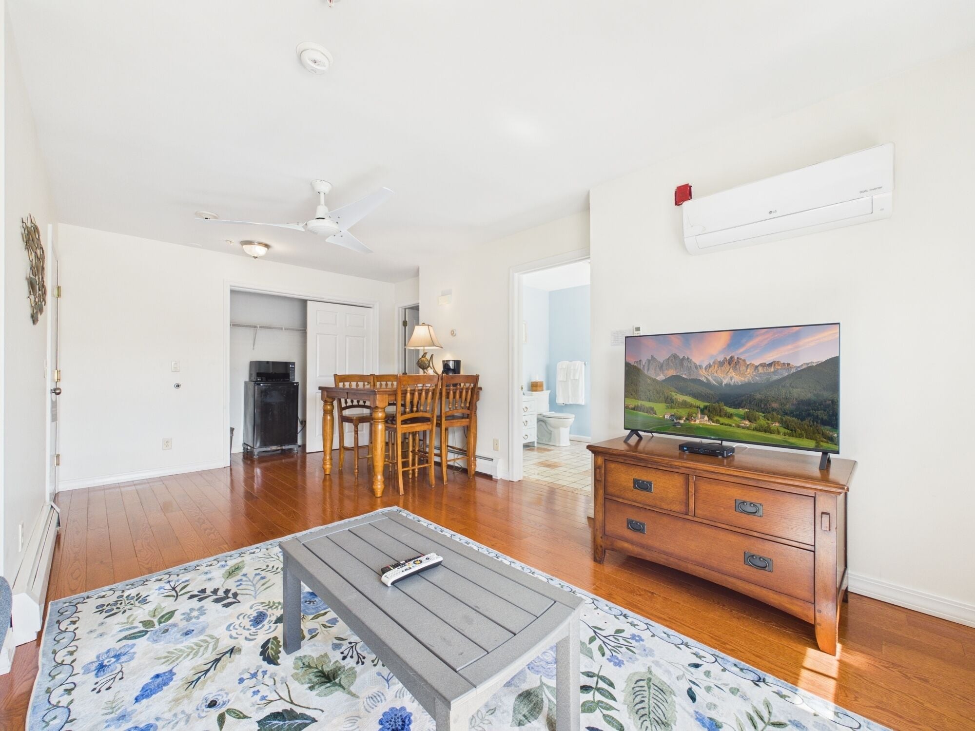A living room with a TV, wooden furniture, a ceiling fan, and a dining area.