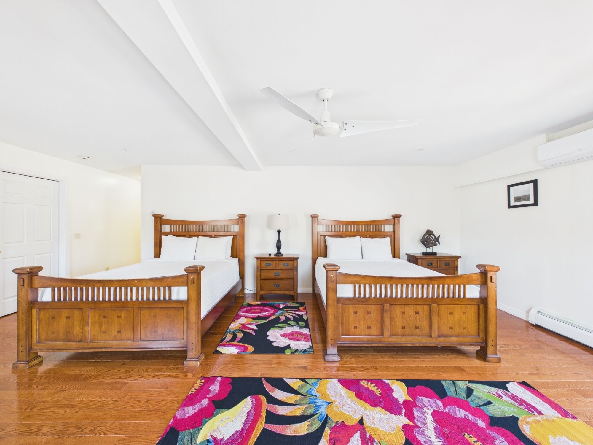 A bedroom with two wooden beds, a ceiling fan, a nightstand, and a floral rug.