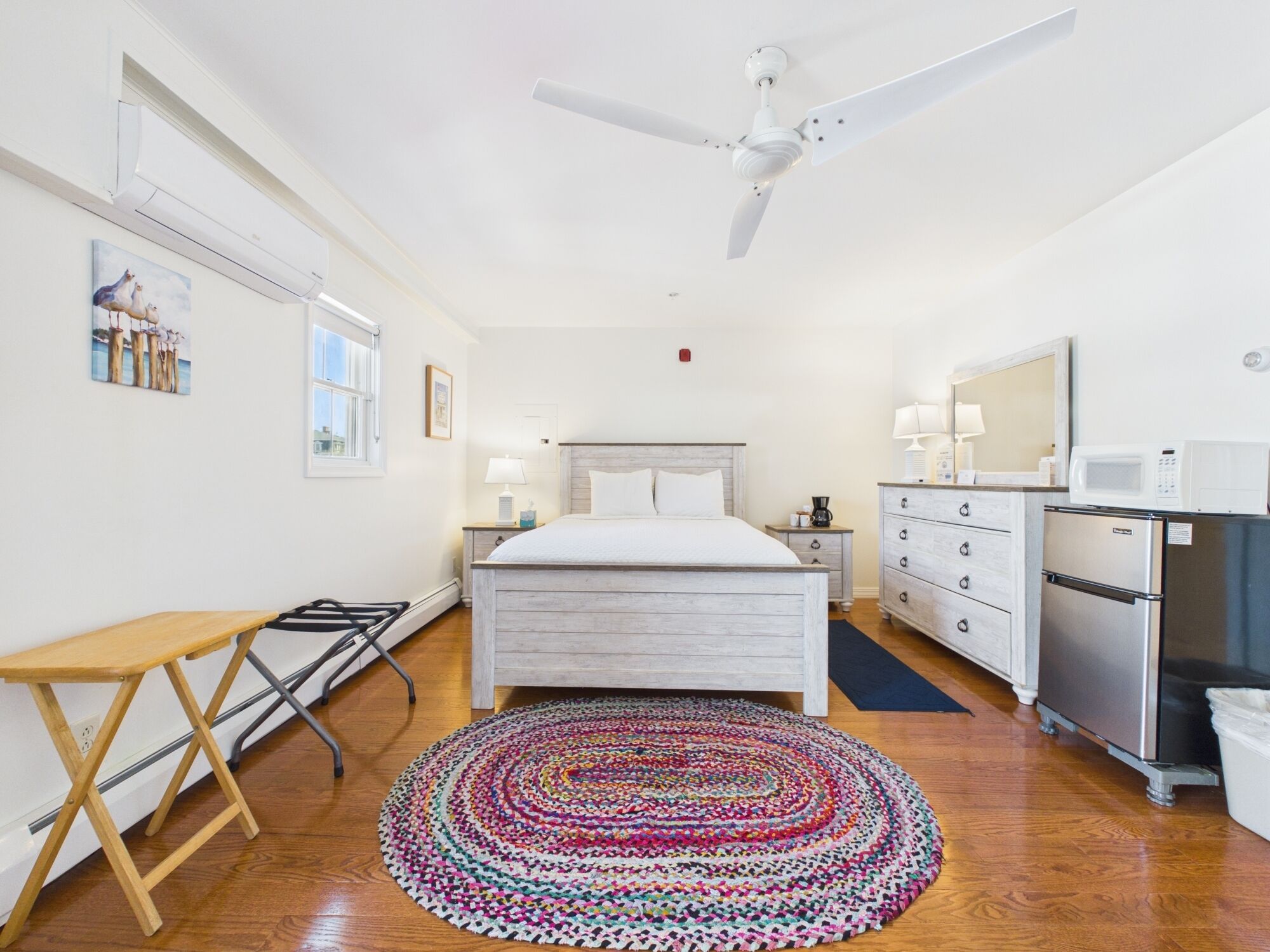 Une chambre à coucher comprenant un lit, un bureau, une chaise, un ventilateur de plafond, une commode, un four à micro-ondes et un réfrigérateur.