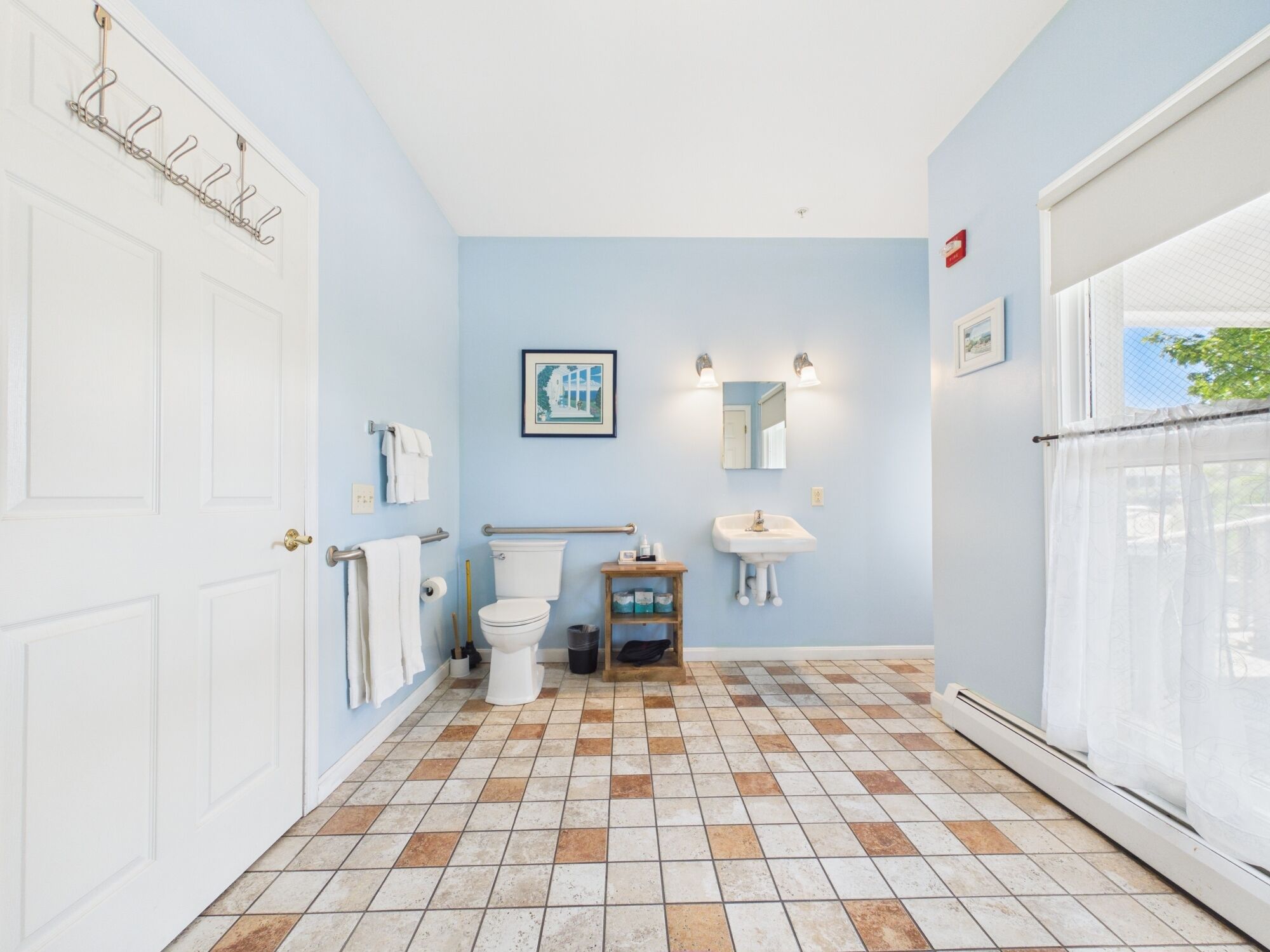 A bathroom with a white door, a toilet, a sink, a towel rack, and a framed picture on the wall.