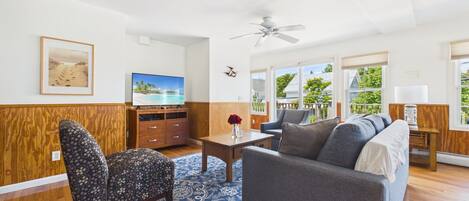 A living room with a television, a ceiling fan, and a view of the outdoors.
