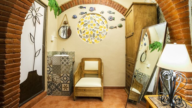 A bathroom with a wooden chair, a sink with patterned tiles, a mirror, and decorative fish on the wall.