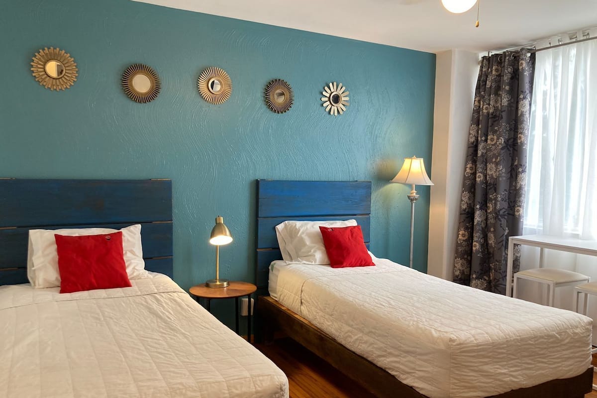 Habitación de hotel con dos camas, una pared de acento color turquesa y apliques decorativos.