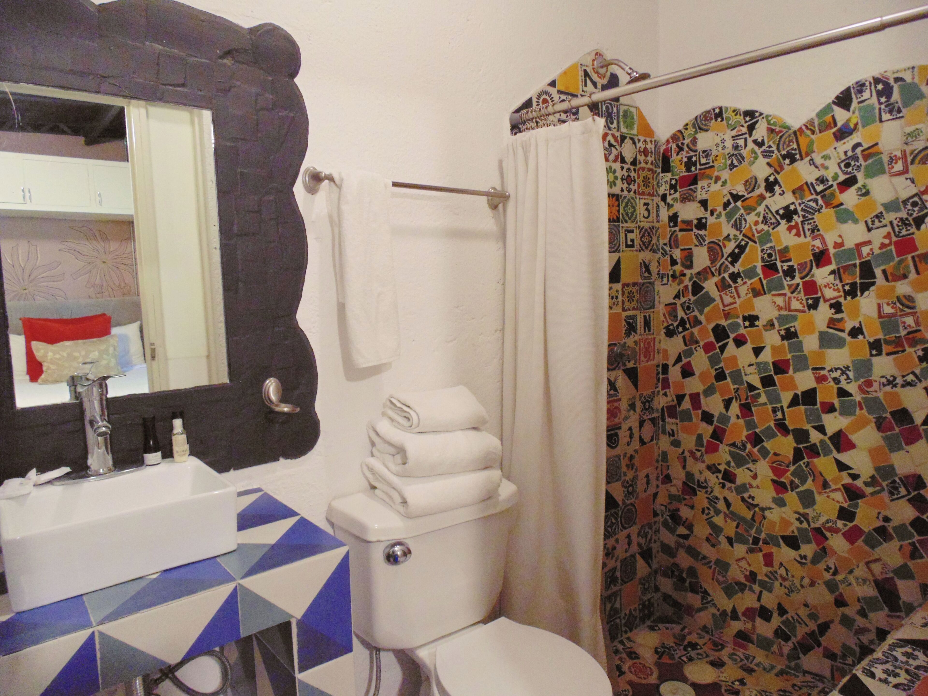 Un baño con lavamanos blanco, inodoro y cortina de ducha con diseño de mosaico.