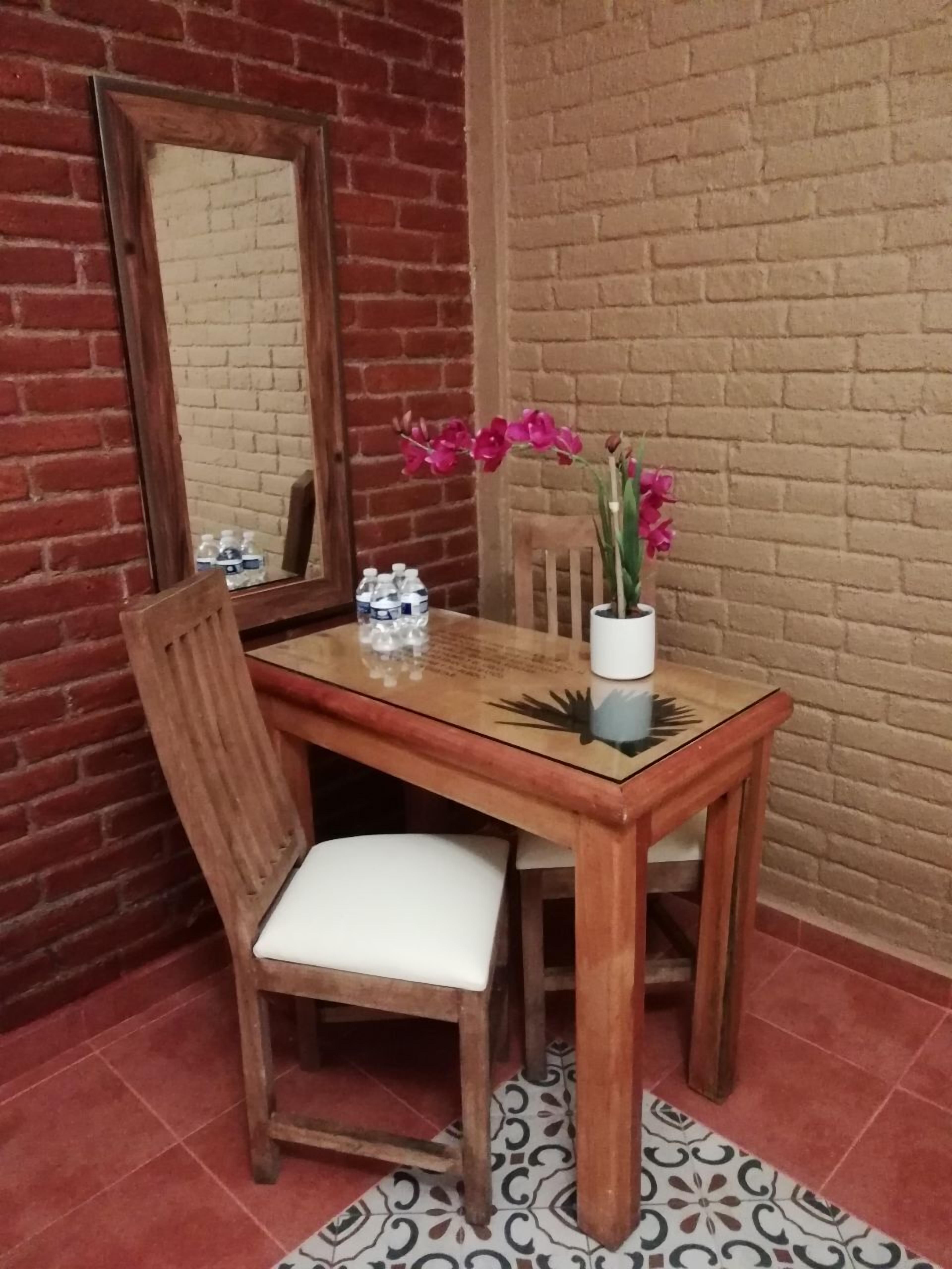 Una mesa de comedor de madera con una silla blanca, un jarrón con flores rosas, un adorno pequeño y un espejo en la pared.