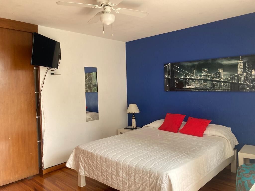 Ein Schlafzimmer mit einem Bett, einem Deckenventilator, einem an der Wand montierten Fernseher und einem Stadtbildgemälde.