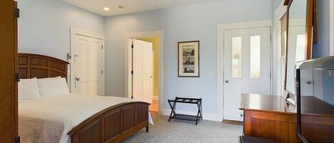 A bedroom with a bed, a desk, a chair, a dresser, and a door.